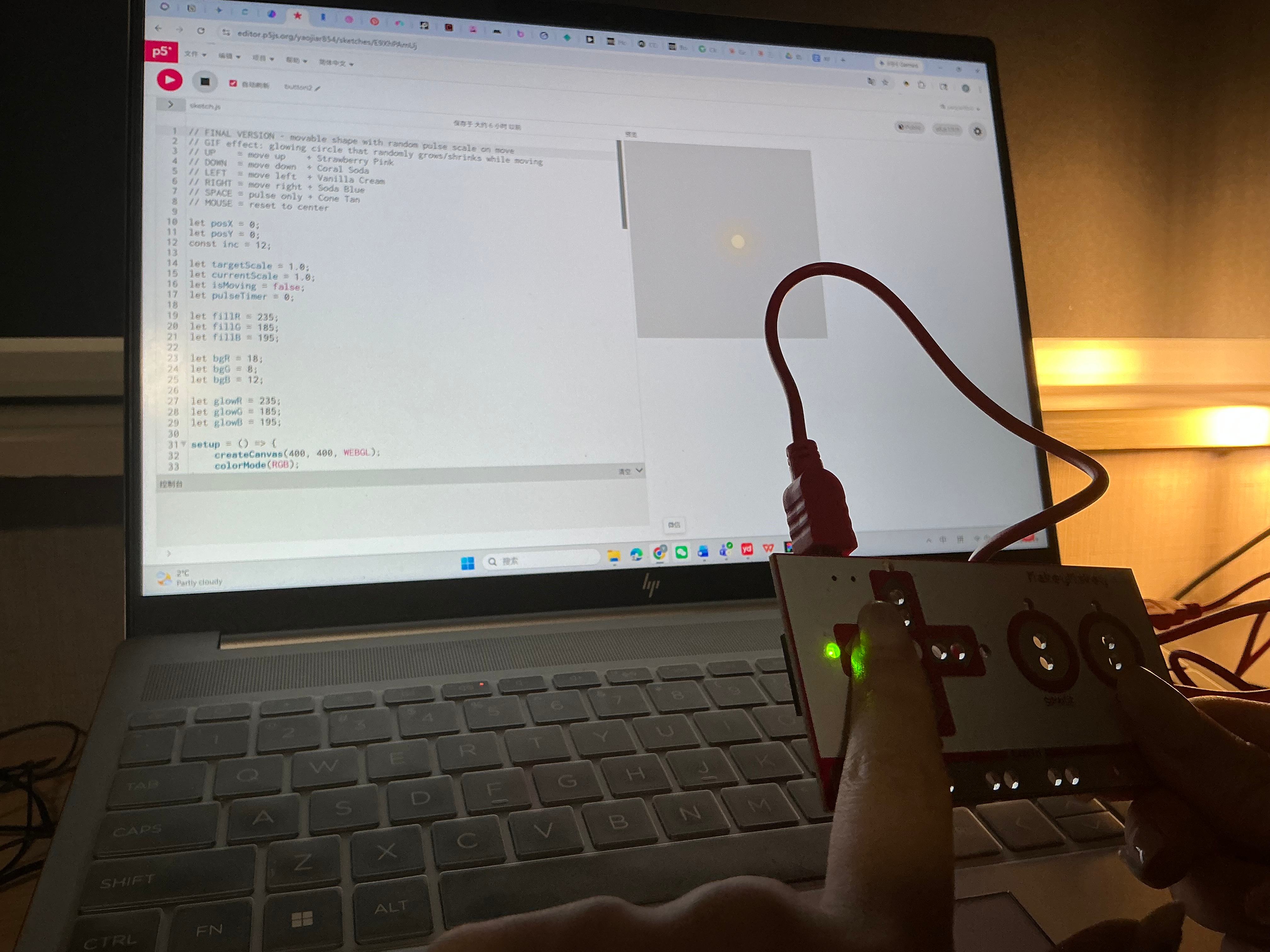 Hand holds Makey Makey while the laptop screen shows a dark canvas with a glowing amber ripple.