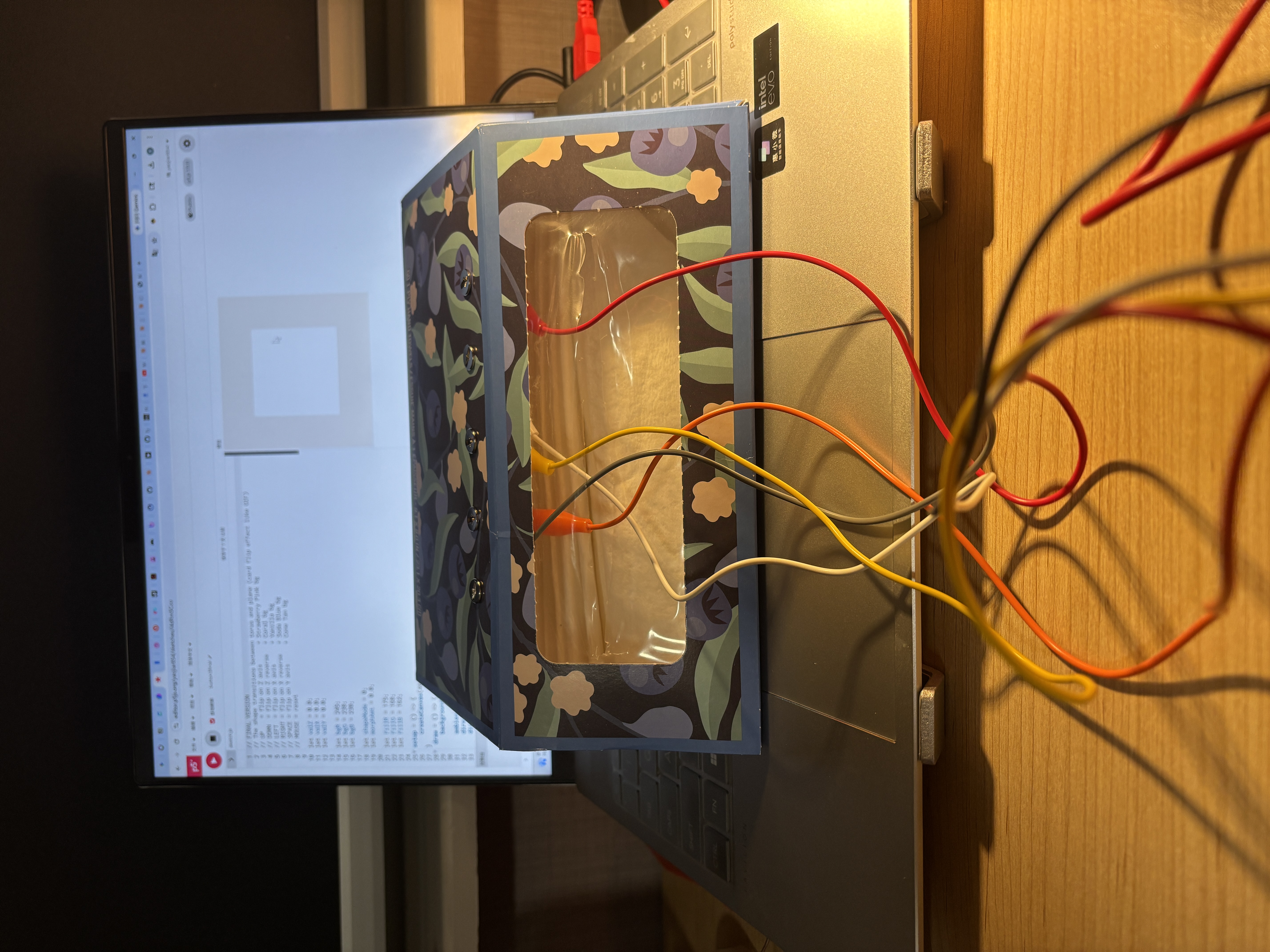 The image displays a floral-patterned box connected to the Makey Makey via colored wires resting on a laptop keyboard, using iron wire loops as the five conductive input buttons.