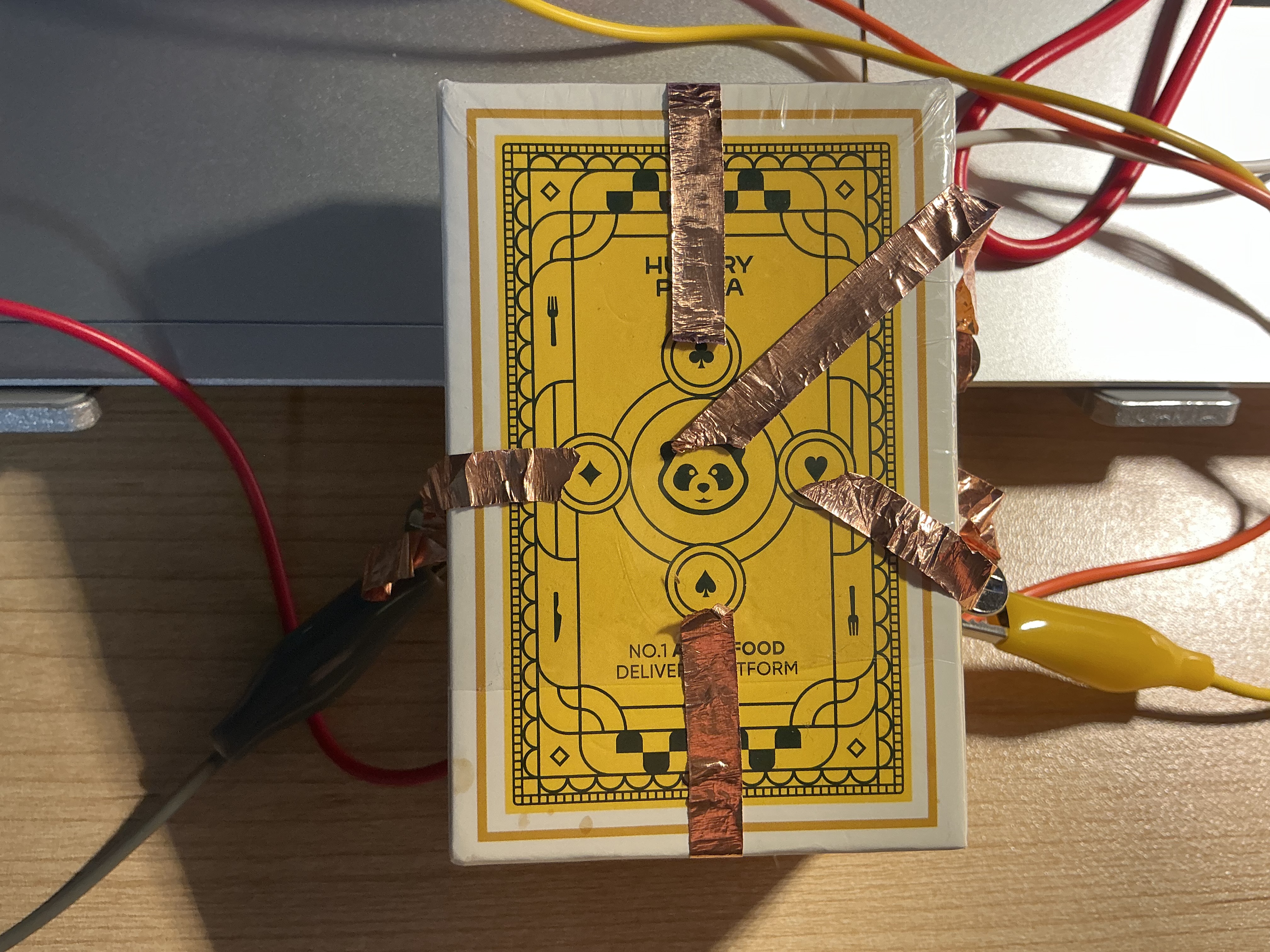 The image displays the yellow Hungry Panda takeout box with copper tape strips arranged in a directional cross pattern and alligator clips attached at each end, using copper tape as the five conductive button zones.